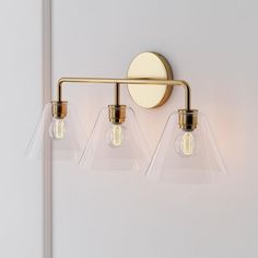 three light bathroom fixture with clear glass shades and brass finish, on white wall background