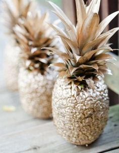 two gold pineapples sitting on top of a wooden table next to each other