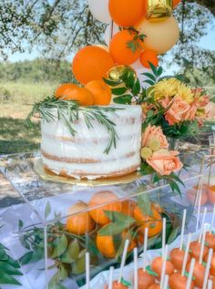 there is a cake on the table with oranges and flowers next to each other