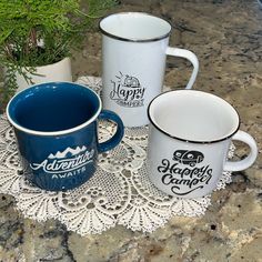 three coffee mugs sitting on top of a doily next to a potted plant