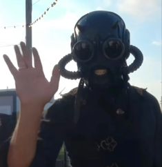 a man in a gas mask and goggles holds his hand up to the camera