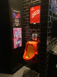 an orange urinal in a public restroom with posters on the wall and toilet paper dispenser