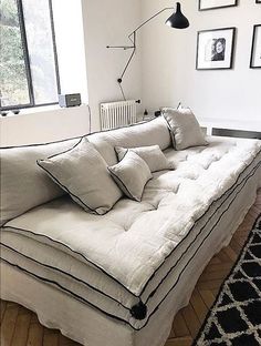 a white couch with pillows on it in front of a window and pictures on the wall