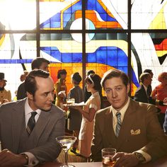 three men sitting at a table in front of a stained glass window with the words mad men on it