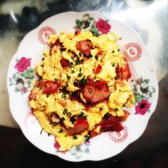 scrambled eggs and strawberries on a white plate with red flowered trim around the edges