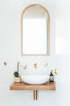 a bathroom sink sitting under a mirror on top of a wooden counter next to a potted plant