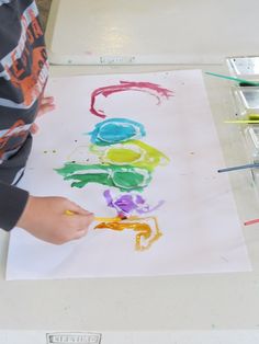 a young boy is drawing on paper with colored crayons and watercolors