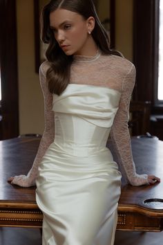 a woman in a white dress sitting at a table with her hands on her hips