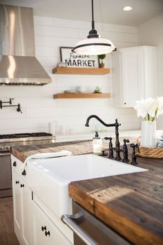 a kitchen with white cabinets and wooden counter tops, an island sink and black faucet