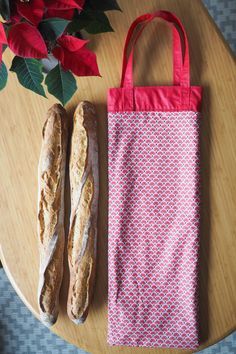 two baguettes sitting on top of a wooden table next to a paper bag