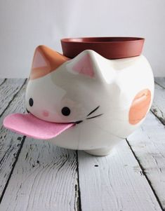 a white ceramic cat planter with a pink hat on it's head sitting on a wooden table