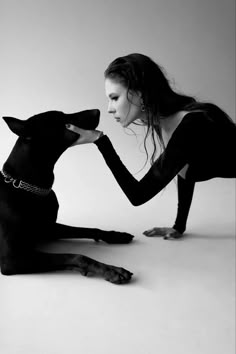 a woman kneeling down next to a black dog