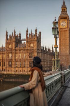 a woman is standing on a bridge looking at the clock tower in london, england