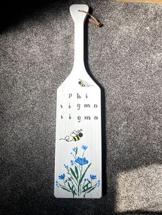 a wooden spoon with flowers and bees on it sitting on the ground next to a wall