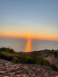 the sun is setting over the ocean and sand dunes