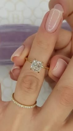 a woman's hand holding a ring with a diamond on it and the other hand