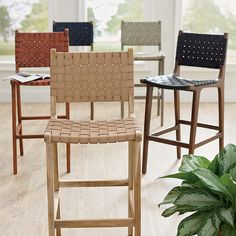 four different colored barstools in front of a large window with potted plant