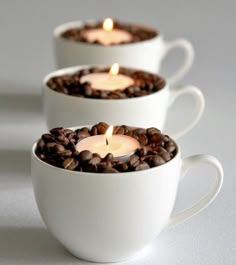 three coffee cups filled with beans and lit candles