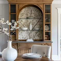 a dining room table with plates and vases on the china cabinet in front of it