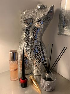 an assortment of beauty products displayed on a table with a mirror behind the statue and candle holder