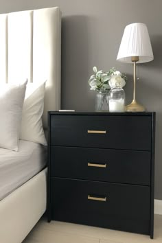 a bedroom with a white bed, black dresser and lamp on top of the night stand