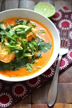 a white bowl filled with soup and garnished with cilantro, parsley and lime