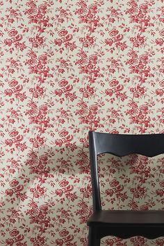 a chair sitting in front of a wall with red and white flowers on the wall