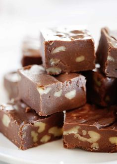 a pile of chocolate fudges on a white plate with other pieces stacked up in the background