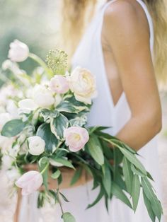 a woman holding a bouquet of white and pink flowers with greenery in her hands