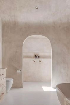 a white bathroom with an arched doorway leading to the toilet and bathtub in it