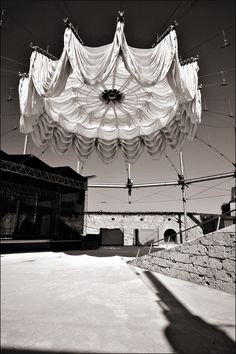 the shadow of a person standing under a white tarp over an outdoor area with stone walls