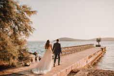 a bride and groom are walking on the pier by the water at their wedding ceremony