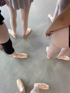 several pairs of ballet shoes are arranged in a circle on the floor as people stand around