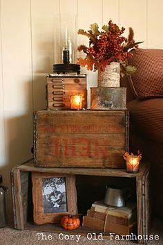 a stack of crates with candles and pictures on them in front of a couch, next to a coffee table