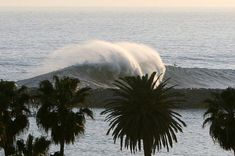 a large wave is coming in from the ocean with palm trees around it and people watching