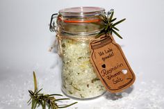 a jar filled with sea salt next to two rosemary sprigs