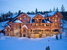 a large wooden house with lots of windows in the middle of snow covered ground and trees