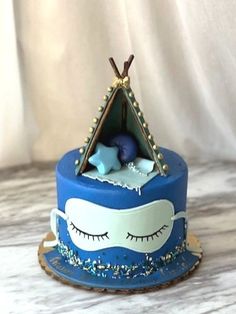 there is a blue cake with a tent on the top and eyes painted on it