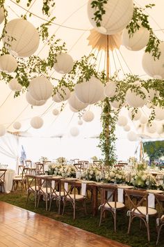 a large tent with tables, chairs and paper lanterns hanging from the ceiling