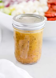 a glass jar filled with mustard sitting on top of a table next to a salad