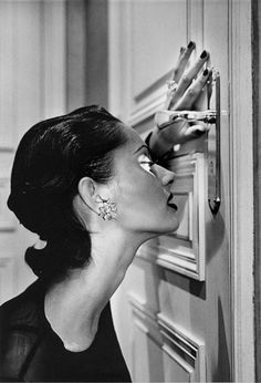 a black and white photo of a woman with her hand on the door knobs