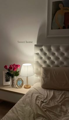 a bedroom with a white bed and pink flowers on the nightstand next to the lamp