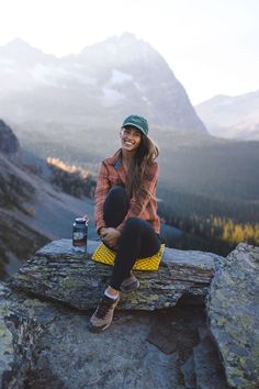 a woman sitting on top of a rock next to a mountain