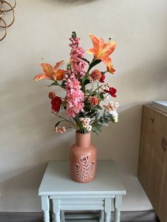 a vase filled with flowers sitting on top of a small table next to a wall