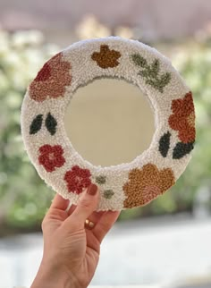 a hand holding up a decorative mirror with flowers on it