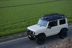 a white jeep driving down a road next to a lush green field