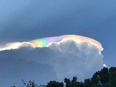 a rainbow appears in the sky above some trees and clouds as it peeks out from behind a cloud