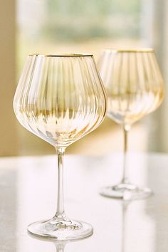 two wine glasses sitting on top of a white table next to each other, one filled with liquid and the other empty