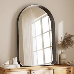 a mirror sitting on top of a wooden dresser next to a white vase and potted plant