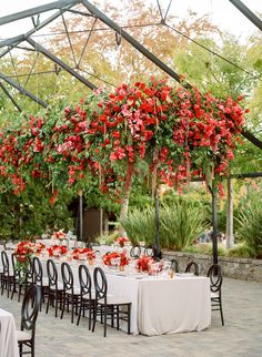 an outdoor dining area with tables and chairs set up for a formal function, covered in red flowers